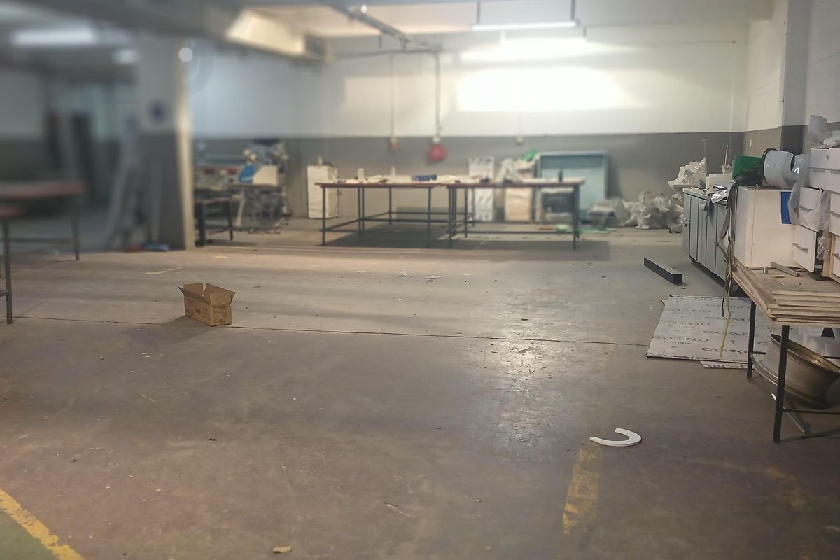 Spacious industrial workshop area featuring high ceilings, fluorescent lighting, and durable concrete flooring, suitable for manufacturing or storage operations.
