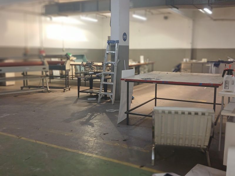 Spacious industrial workshop area featuring high ceilings, exposed ductwork, and durable concrete flooring, suitable for manufacturing or storage operations.