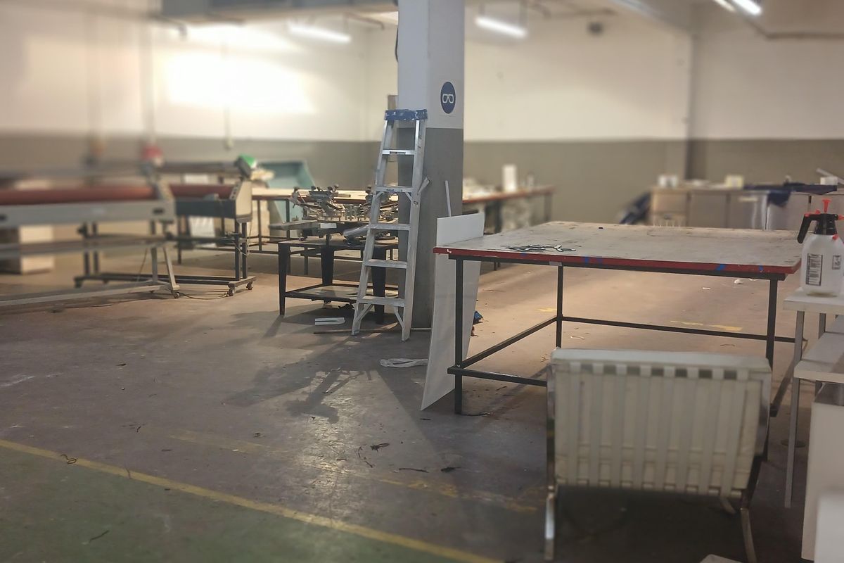 Spacious industrial workshop area featuring high ceilings, exposed ductwork, and durable concrete flooring, suitable for manufacturing or storage operations.
