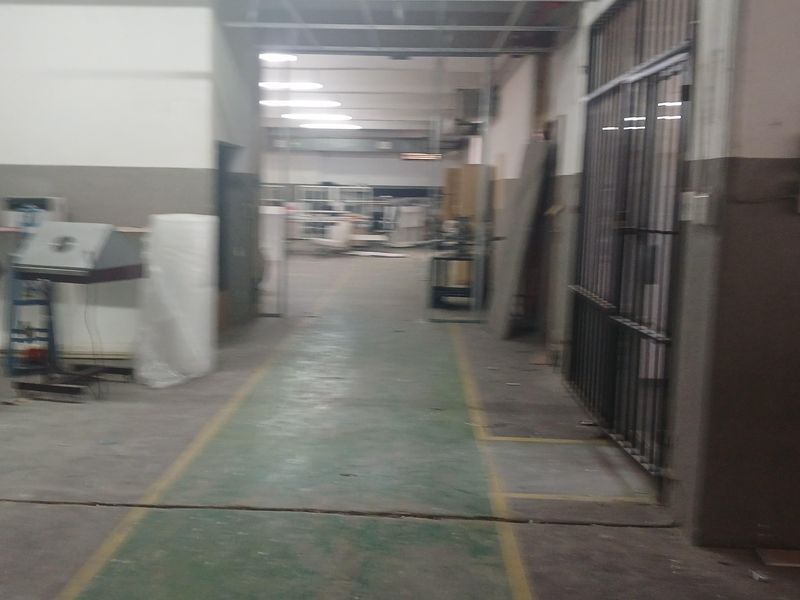 Industrial warehouse interior featuring a concrete floor with safety markings, exposed ceiling structure, and secure metal gate access.