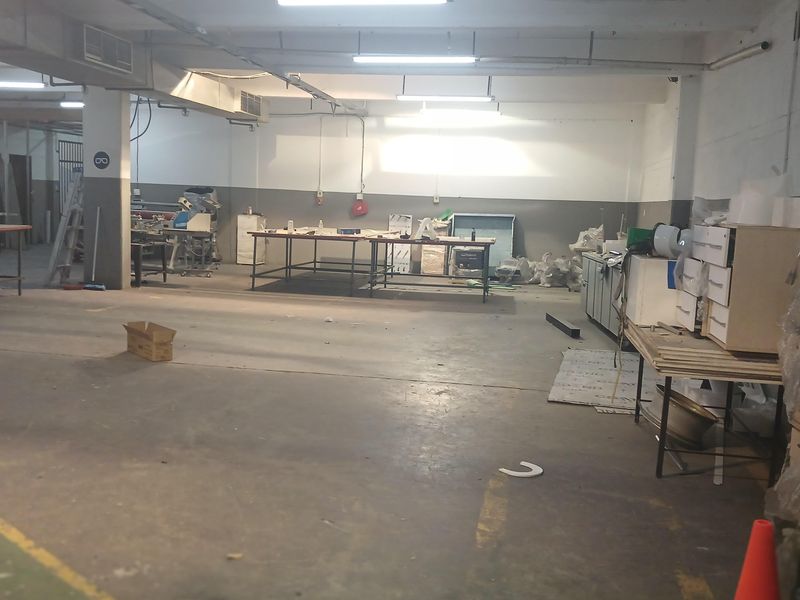 Spacious industrial warehouse or workshop area featuring high ceilings, exposed lighting fixtures, and durable concrete flooring, suitable for various commercial or manufacturing operations.