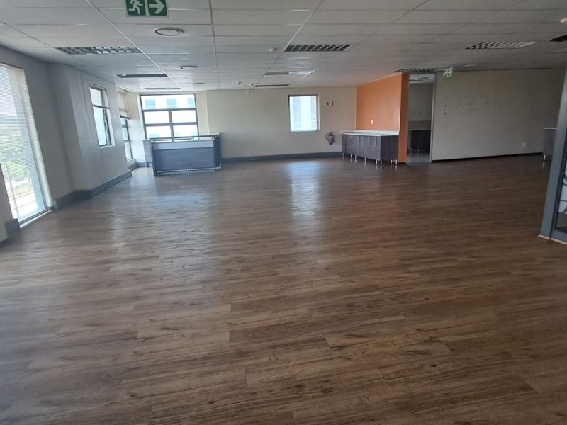 Spacious open-plan office area featuring wood-look laminate flooring, suspended ceiling tiles, and built-in cabinetry, offering a versatile workspace layout.