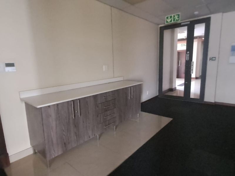 A functional office hallway featuring a built-in storage cabinet with a countertop, dark carpeting, and a glass-paneled emergency exit door.