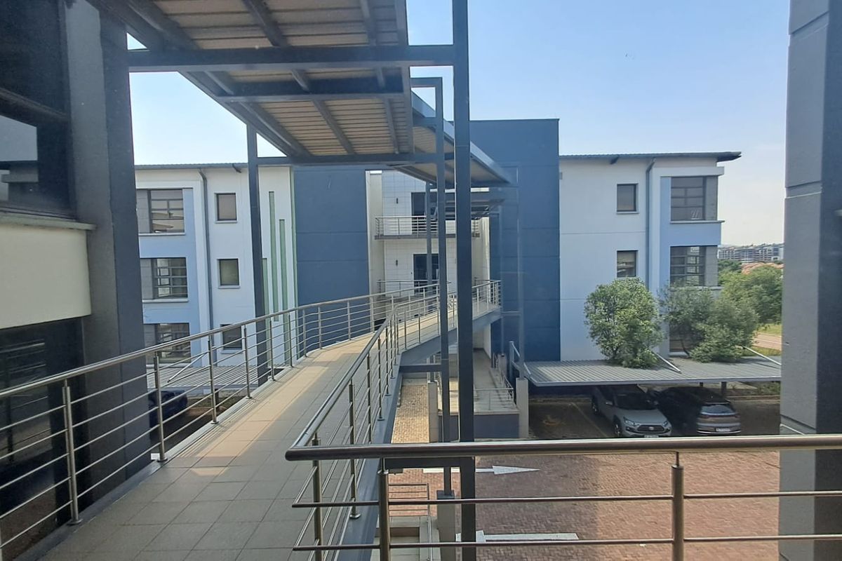 An elevated pedestrian walkway connecting office building wings, featuring modern steel railings and a covered structure overlooking the parking area.
