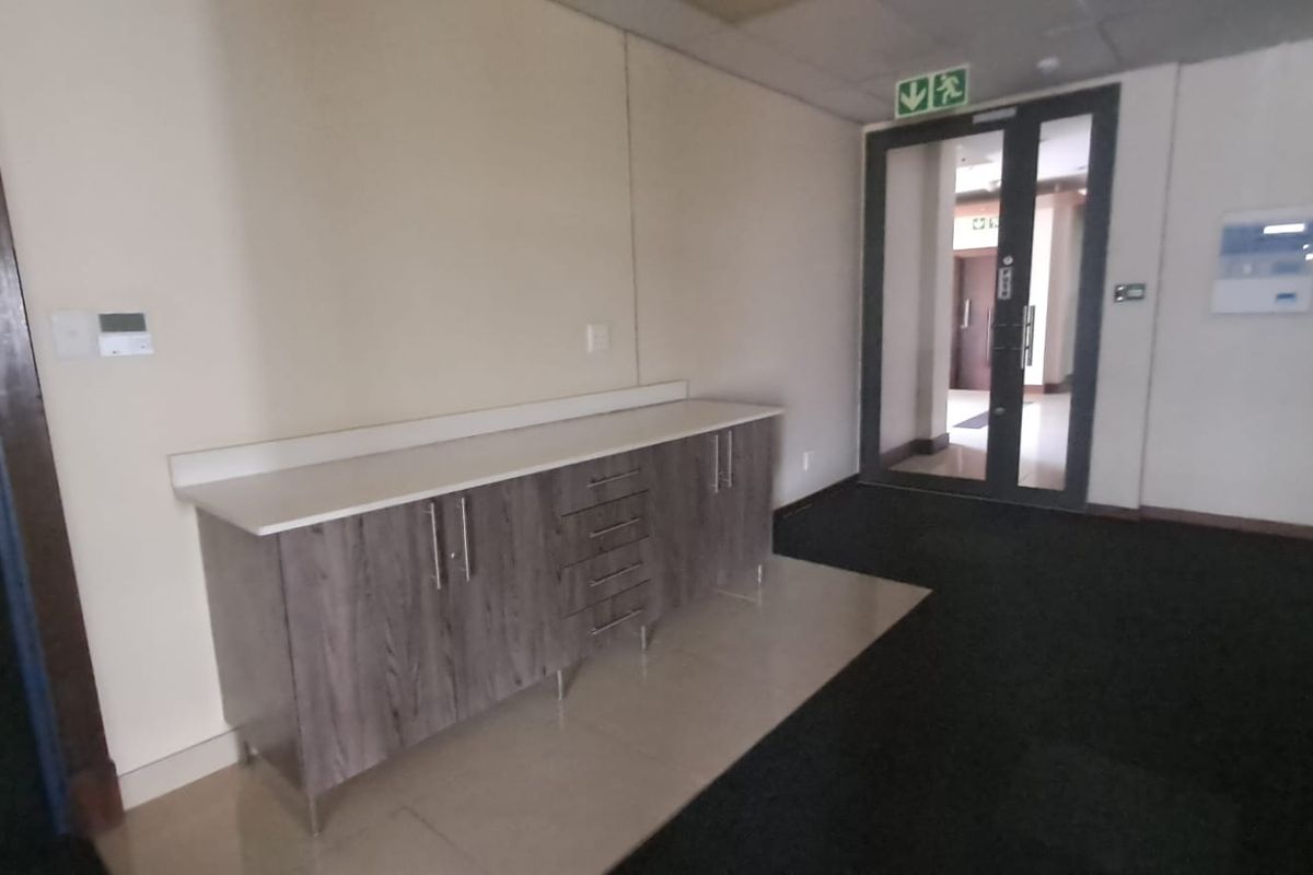 A functional office hallway featuring a built-in storage cabinet with a countertop, dark carpeting, and a glass-paneled emergency exit door.