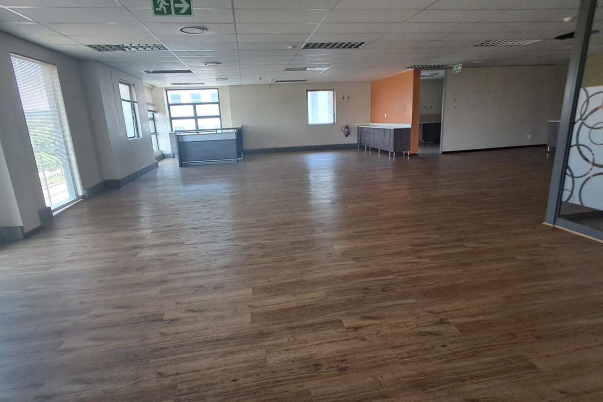 Spacious open-plan office area featuring wood-look laminate flooring, suspended ceiling tiles, and built-in cabinetry, offering a versatile workspace layout.