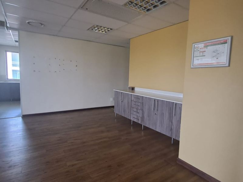 An open-plan office space featuring wood-look flooring, a built-in storage cabinet, and a suspended ceiling with integrated lighting.