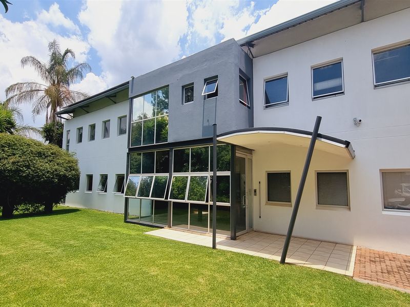 Rear exterior view of the office building featuring a modern glass facade, covered patio area, and well-maintained lawn.