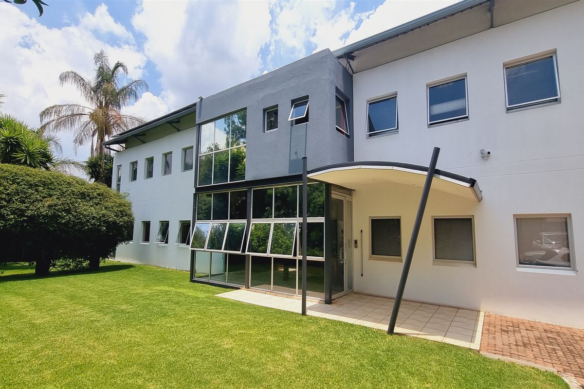 Rear exterior view of the office building featuring a modern glass facade, covered patio area, and well-maintained lawn.