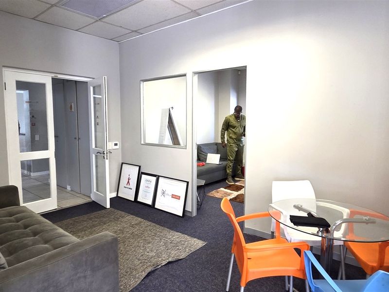 A functional office space featuring carpeted flooring, a suspended ceiling, and a glass partition providing visibility into an adjacent room.