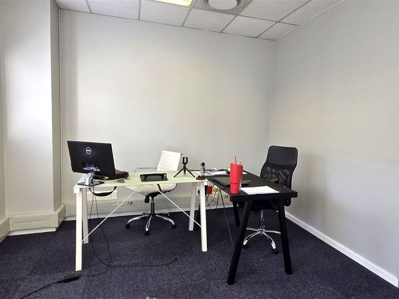 A functional office space featuring a suspended ceiling, recessed lighting, carpeted flooring, and a window with venetian blinds.