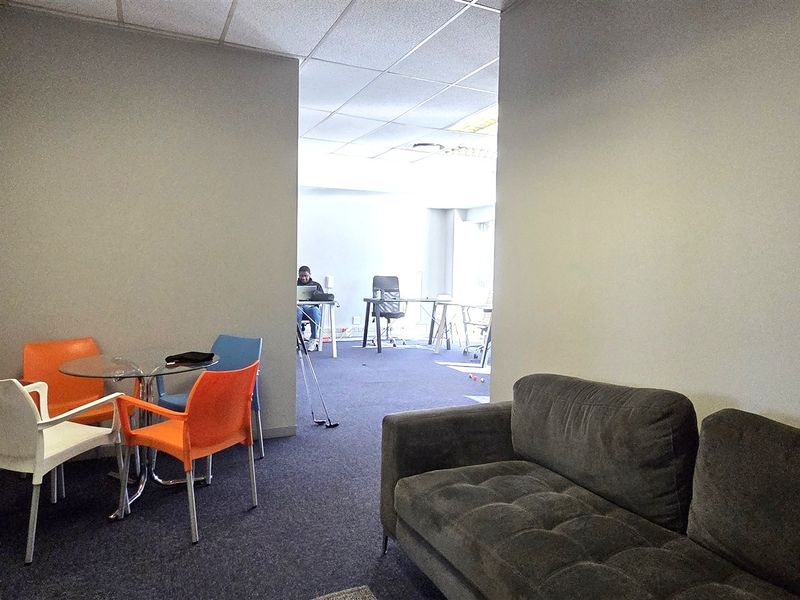 An office space featuring a suspended ceiling and carpeted flooring, providing a functional work environment with a small breakout area.