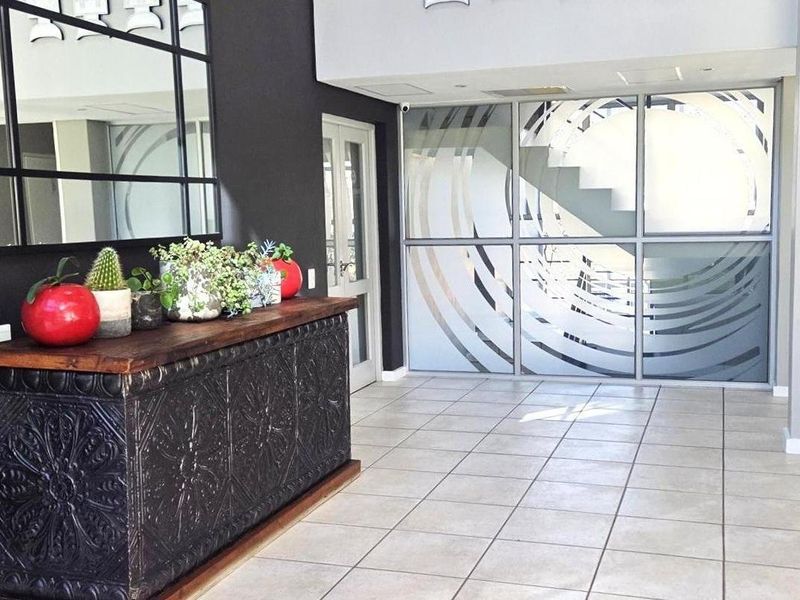 Modern office entrance area featuring tiled flooring, a large decorative mirror, and a contemporary frosted glass partition wall.
