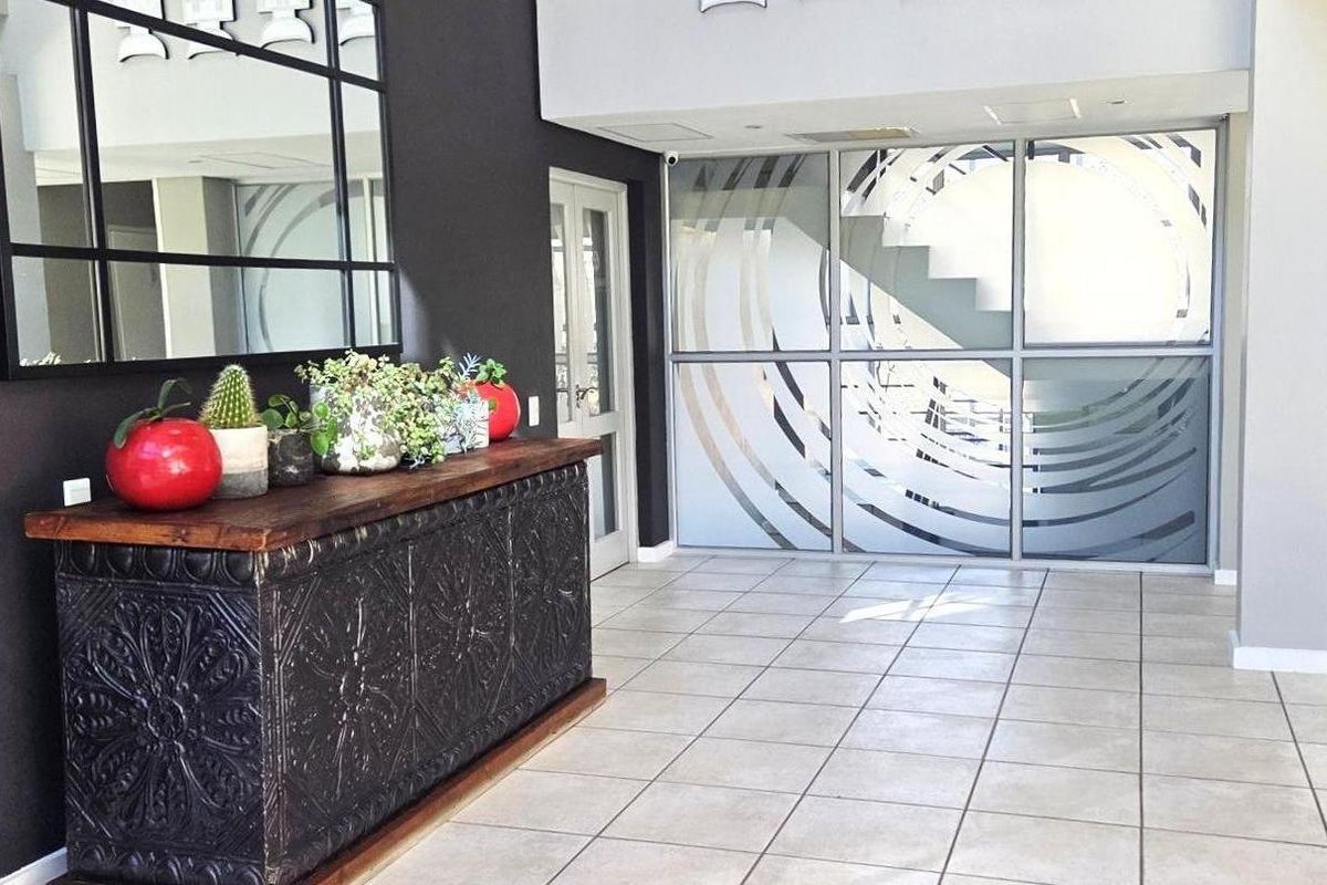 Modern office entrance area featuring tiled flooring, a large decorative mirror, and a contemporary frosted glass partition wall.