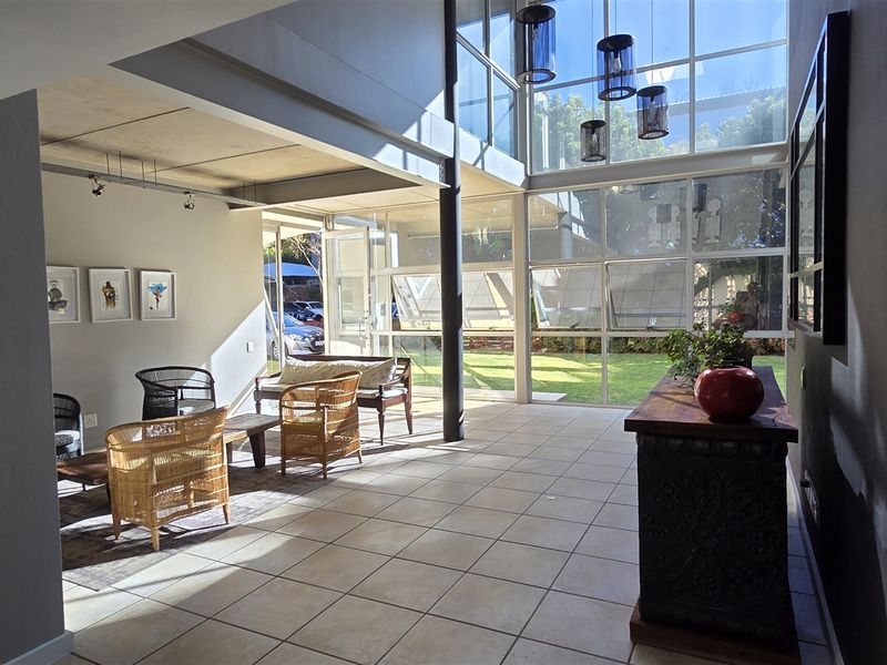 Spacious open-plan office area featuring double-volume ceilings, extensive floor-to-ceiling glass windows, and modern ceramic tile flooring with abundant natural light.