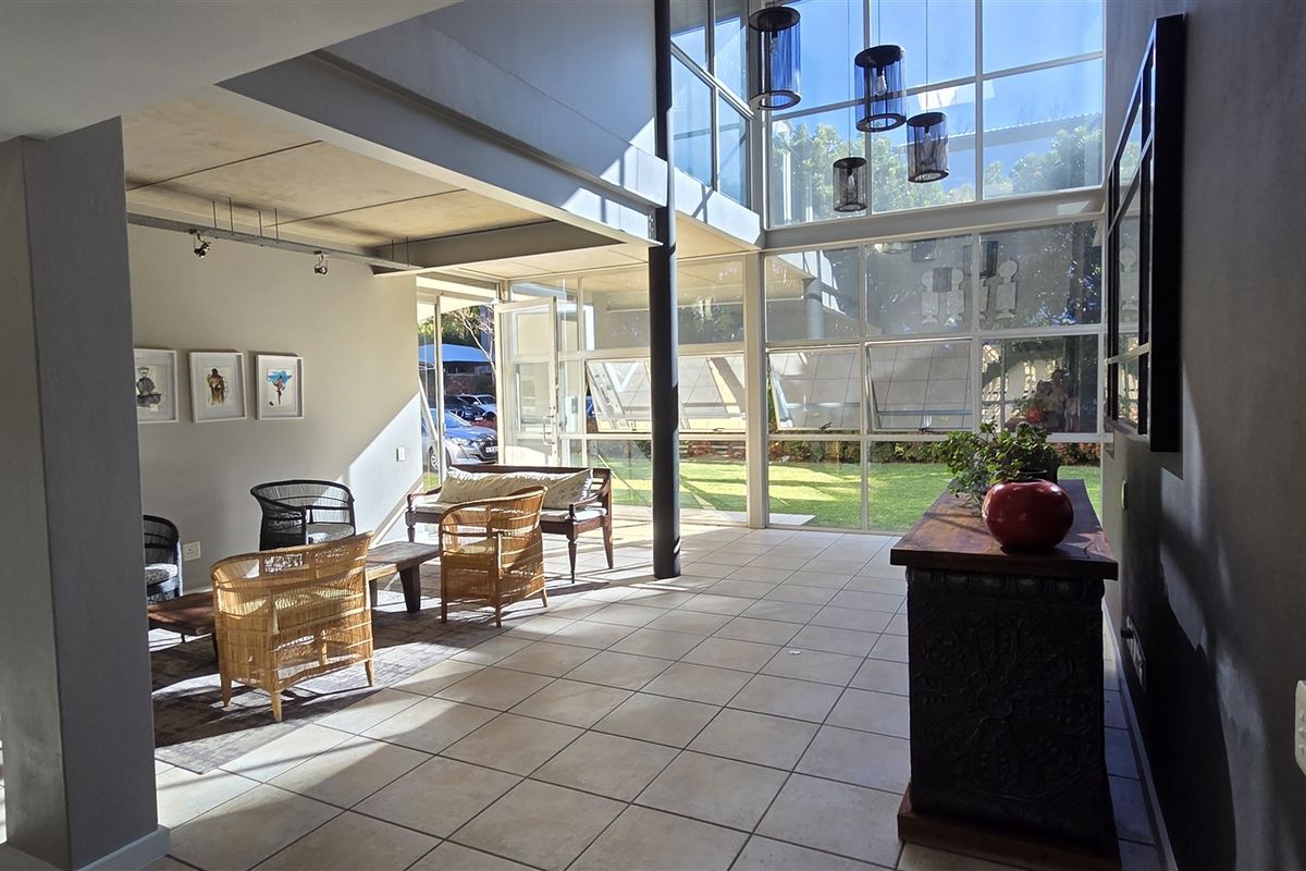 Spacious open-plan office area featuring double-volume ceilings, extensive floor-to-ceiling glass windows, and modern ceramic tile flooring with abundant natural light.