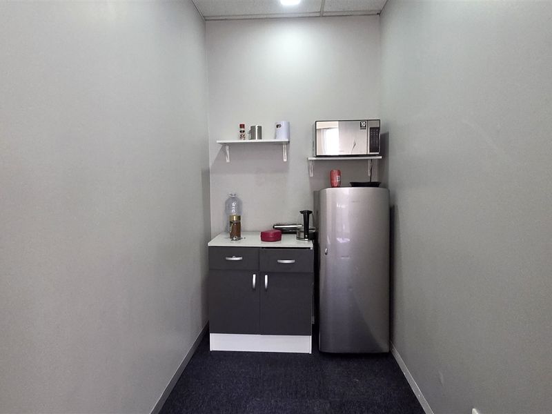 A compact office kitchenette featuring built-in base cabinetry, a countertop, and floating shelving for convenient storage and preparation.