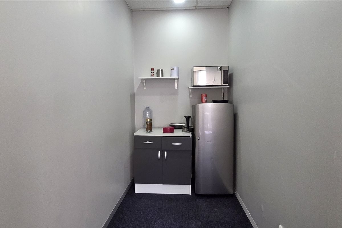 A compact office kitchenette featuring built-in base cabinetry, a countertop, and floating shelving for convenient storage and preparation.