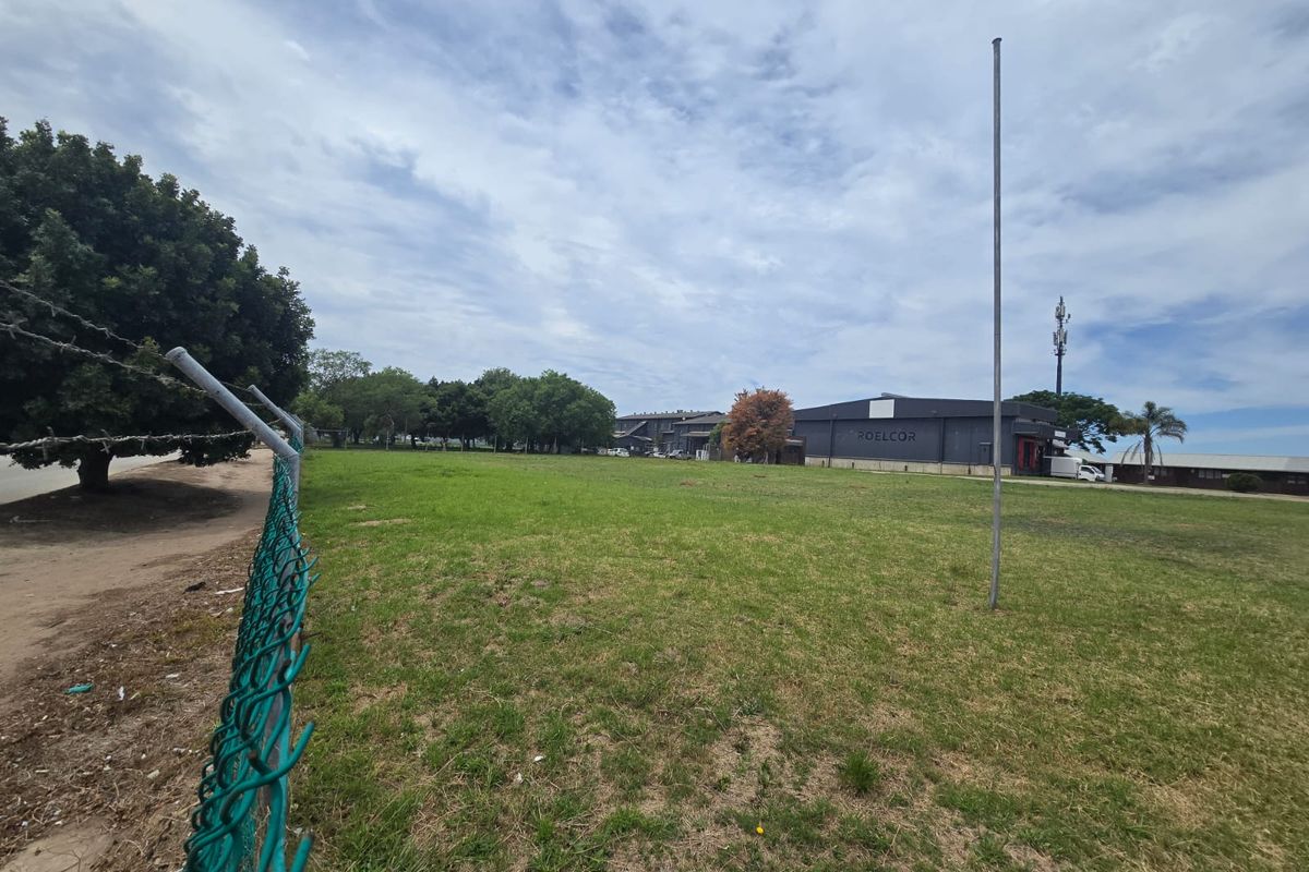 A wide-angle view of a vacant commercial land plot featuring a chain-link perimeter fence and a flagpole.