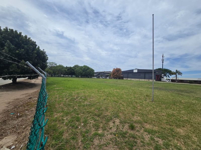 A wide-angle view of a vacant commercial land plot featuring a chain-link perimeter fence and a flagpole.