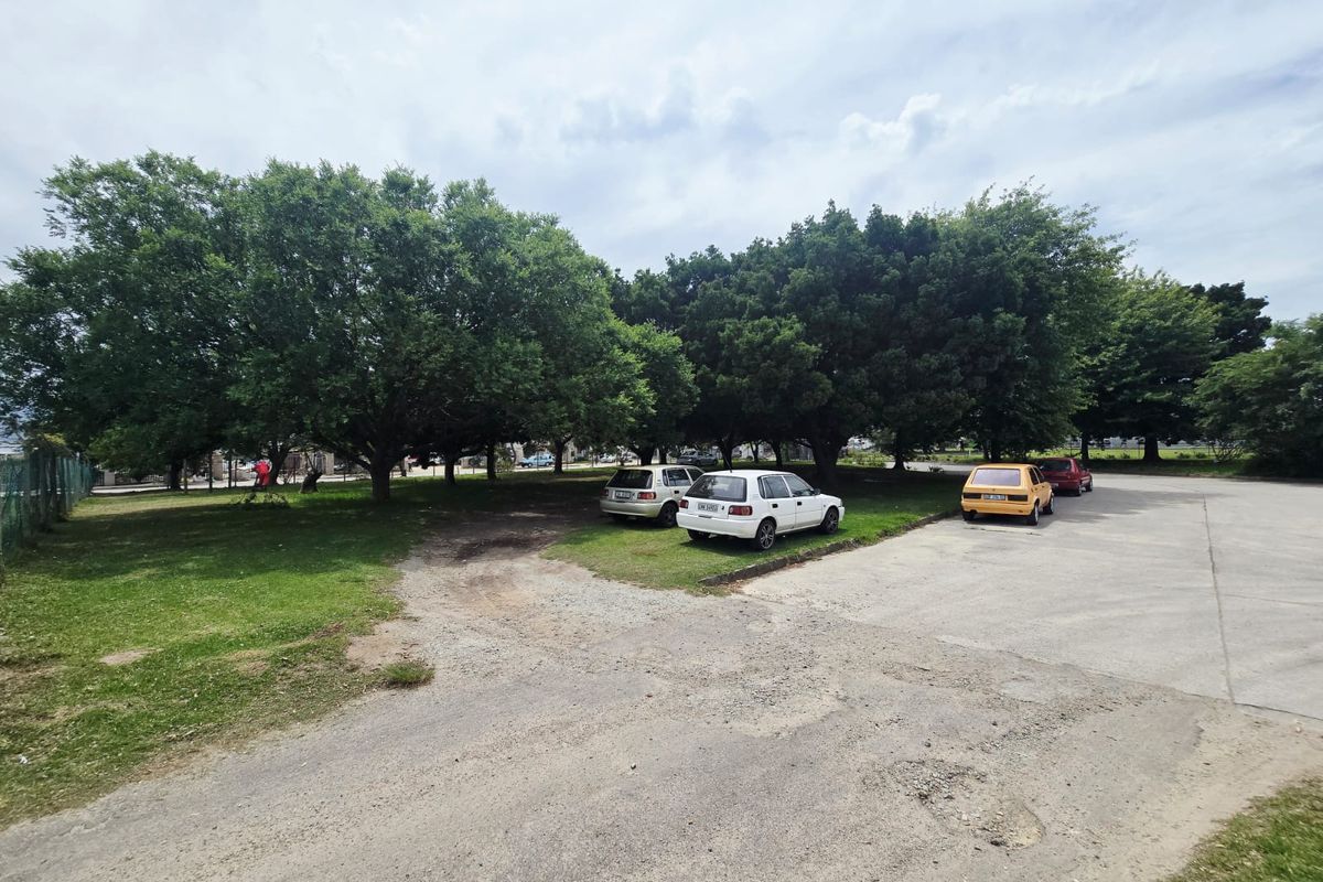 A view of a commercial vacant land plot featuring a concrete driveway, mature trees, and a grass lawn area.