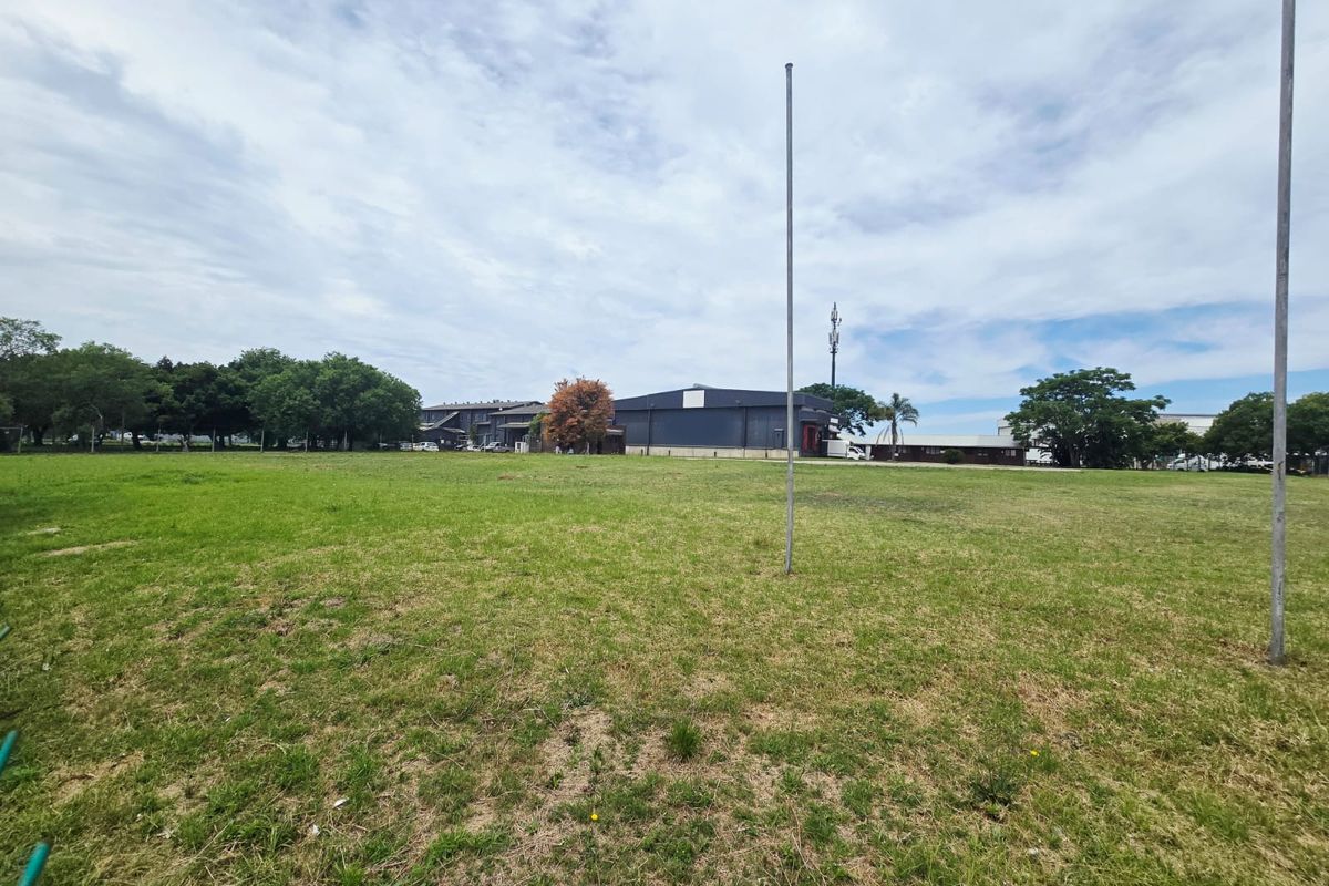 A wide, open grass field on a commercial vacant land plot, featuring a telecommunications mast and surrounding mature trees.