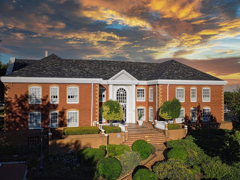 An aerial view of a grand, multi-story brick office building featuring a symmetrical facade, classic multi-pane windows, and a landscaped front entrance.
