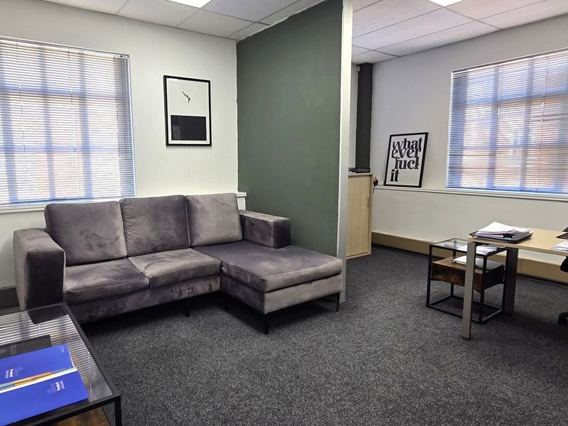 A functional office space featuring a partition wall, carpeted flooring, and large windows with venetian blinds, providing a professional work environment.