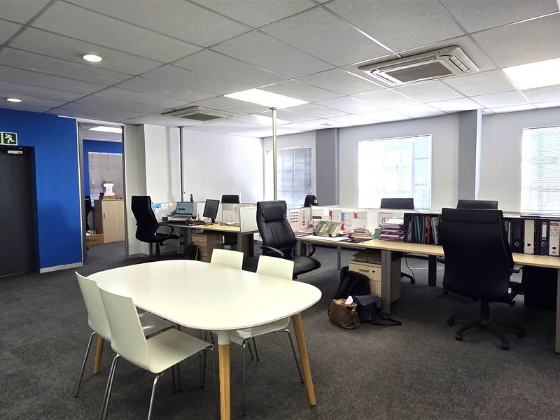 Open-plan office space featuring suspended ceilings, recessed lighting, integrated cassette air conditioning, and carpeted flooring, providing a functional workspace environment.
