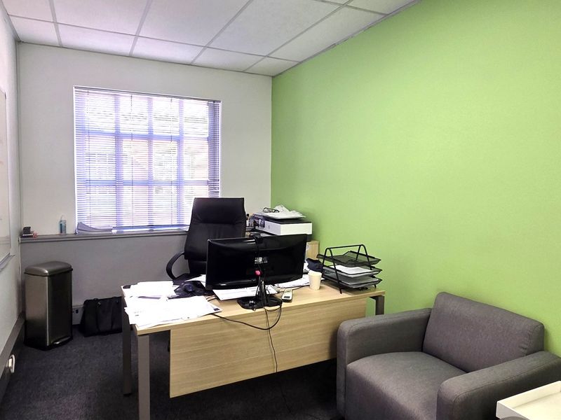A functional office space featuring a suspended ceiling, window blinds, and a large wall-mounted whiteboard, providing a practical work environment.