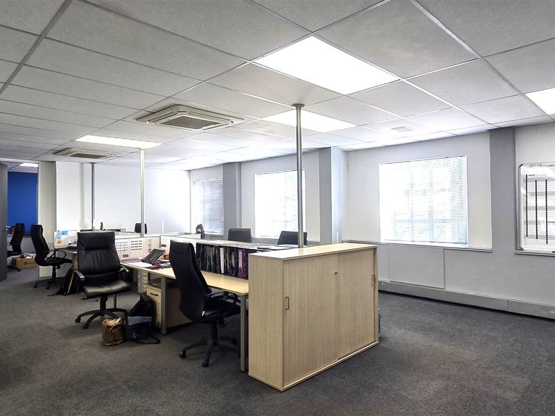 A functional open-plan office space featuring a suspended ceiling, recessed lighting, integrated air conditioning, and carpeted flooring.