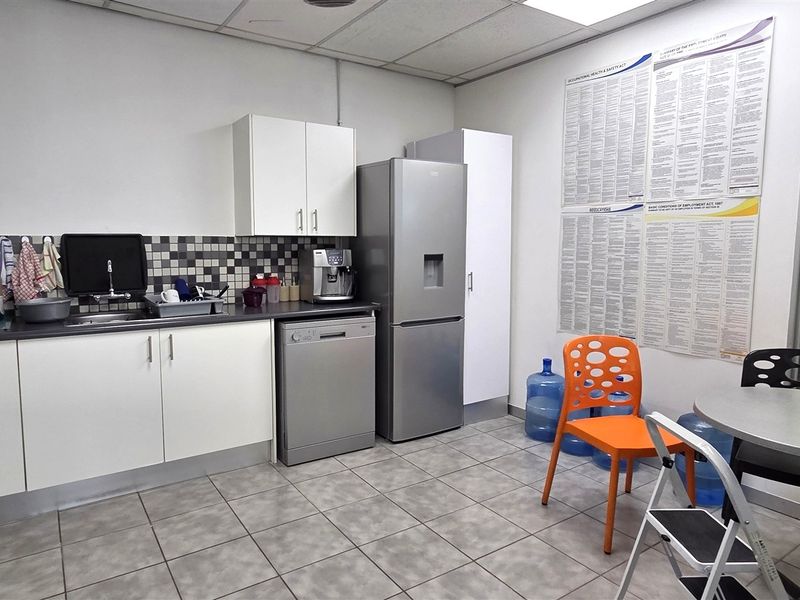 A functional office kitchenette featuring white cabinetry, tiled backsplash, and durable tiled flooring, providing a convenient space for staff refreshments.