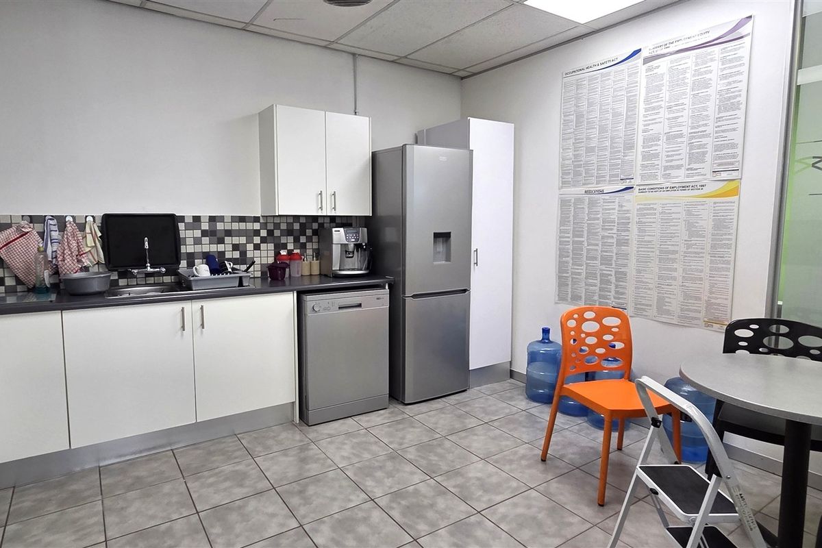 A functional office kitchenette featuring white cabinetry, tiled backsplash, and durable tiled flooring, providing a convenient space for staff refreshments.