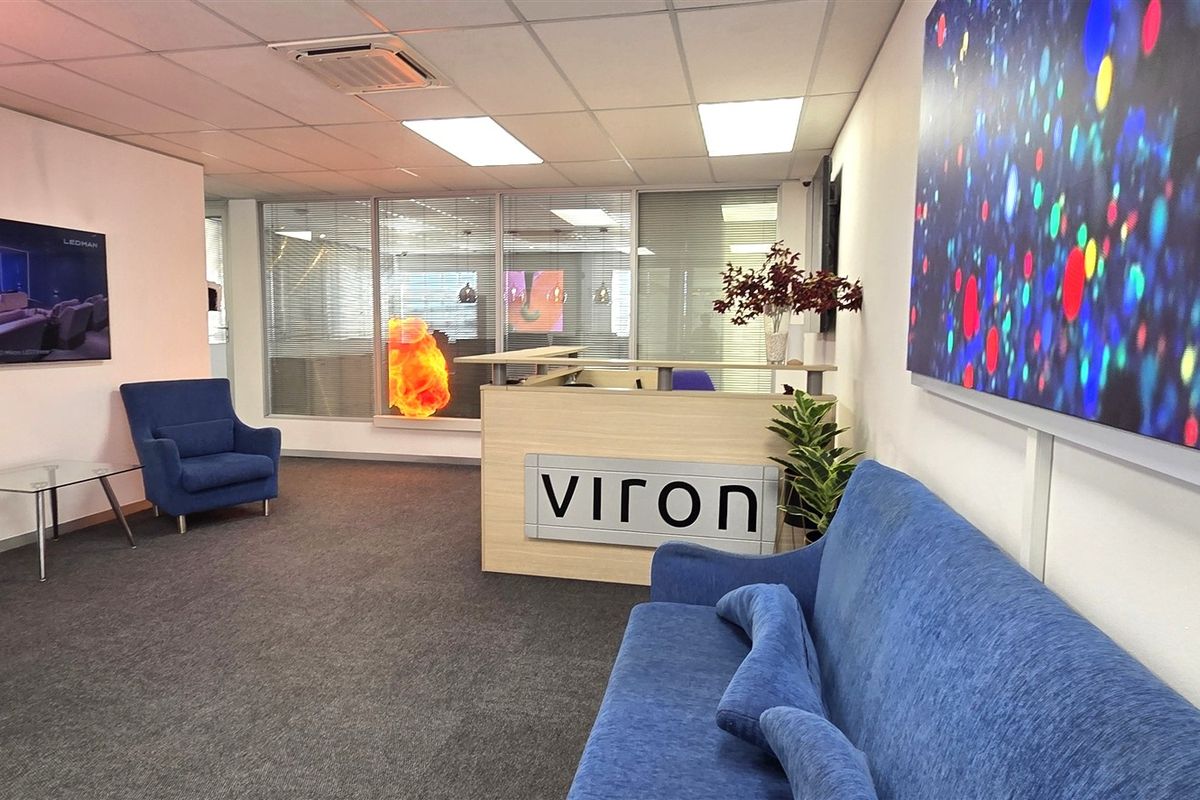Professional office reception area featuring a branded reception desk, glass partitioning, and a clean, modern layout with carpeted flooring.