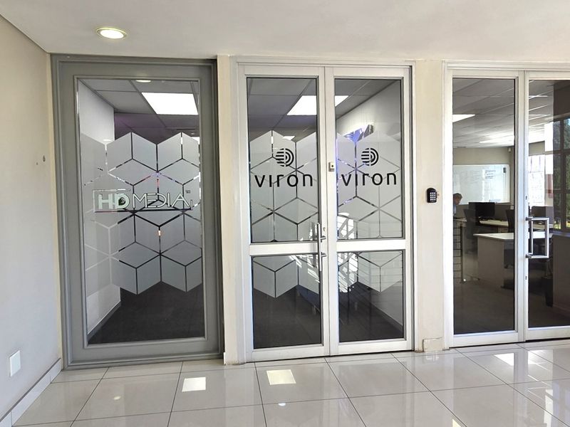 A bright office entrance lobby featuring modern glass partition doors, tiled flooring, and integrated access control systems.