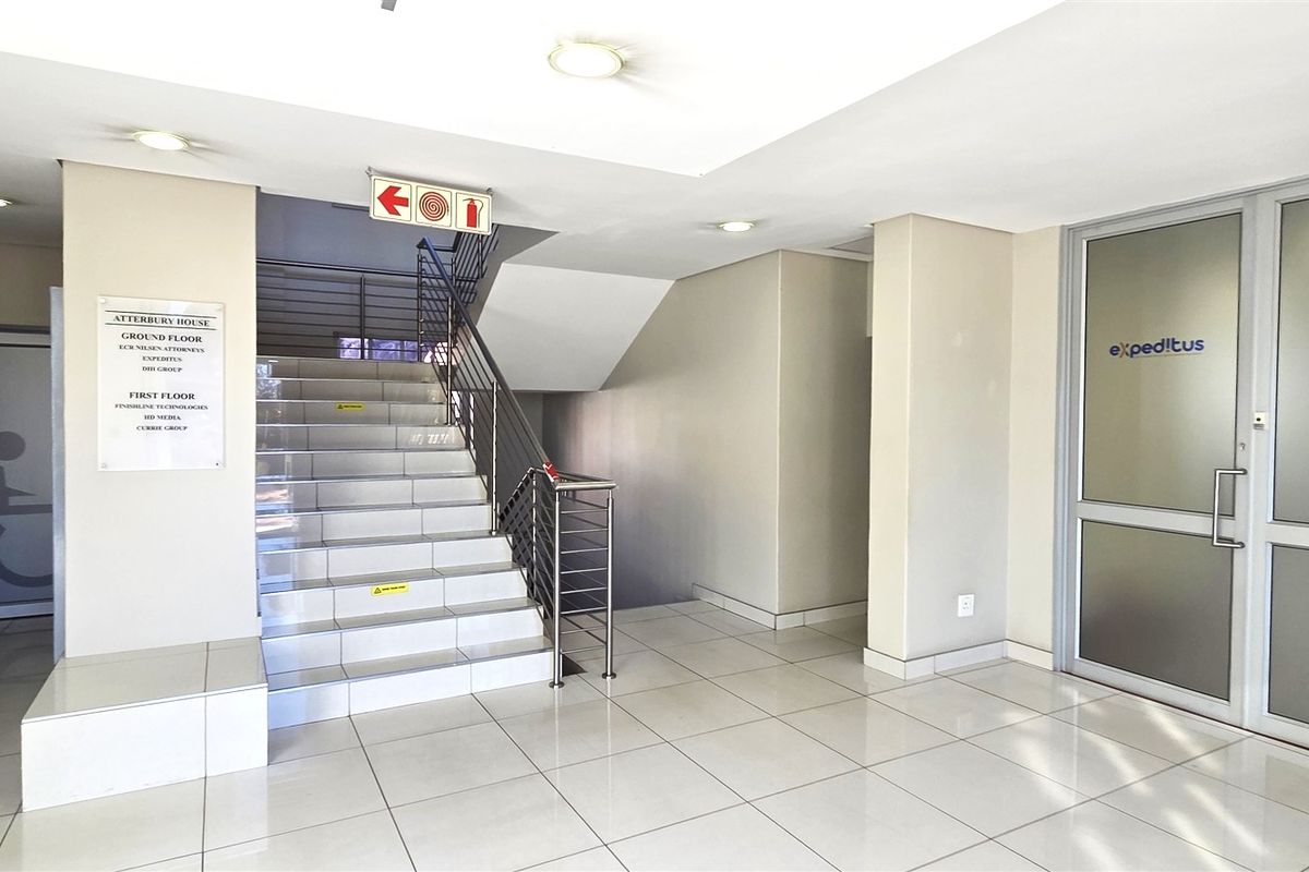 A clean and professional office building entrance lobby featuring tiled flooring, a central staircase, and glass-paneled office access doors.