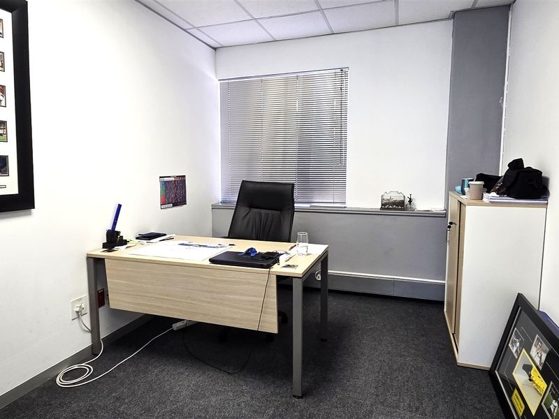 A functional office space featuring carpeted flooring, a suspended ceiling, and window blinds, providing a professional environment for work.