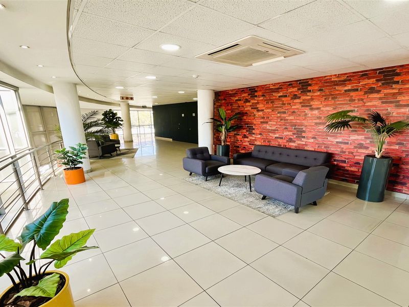 Modern office reception or breakout area featuring a striking brick feature wall, tiled flooring, and integrated ceiling air conditioning.