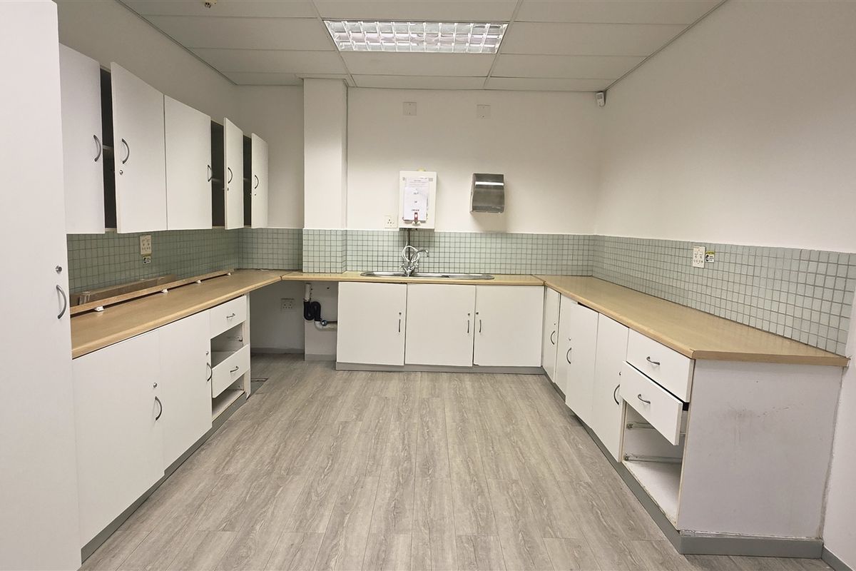 A functional office kitchenette featuring built-in cabinetry, laminate countertops, a stainless steel sink, and tiled backsplash, currently in need of minor repairs and updates.