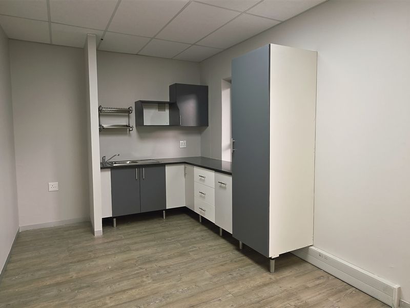 A clean, modern kitchenette area featuring built-in cabinetry, a stainless steel sink, and direct access to an outdoor patio space.