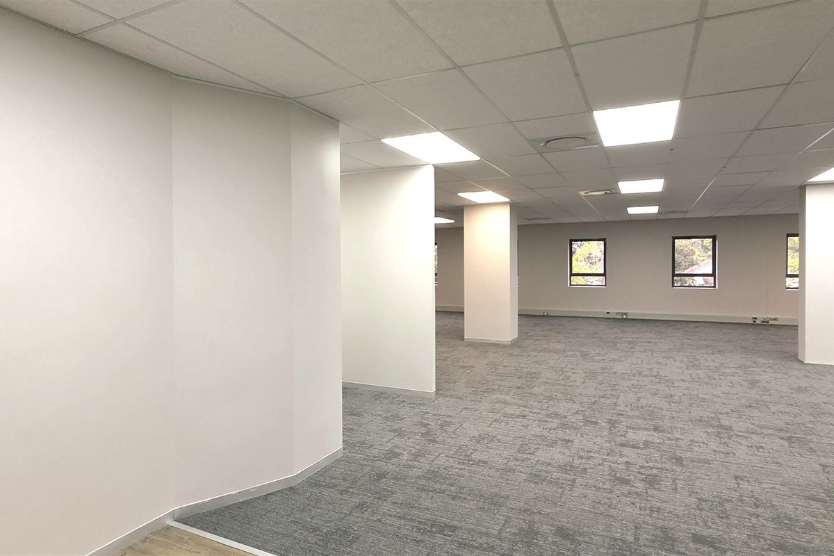A spacious, open-plan office area featuring a suspended ceiling, recessed lighting, and neutral carpet tiles, providing a clean and professional workspace.