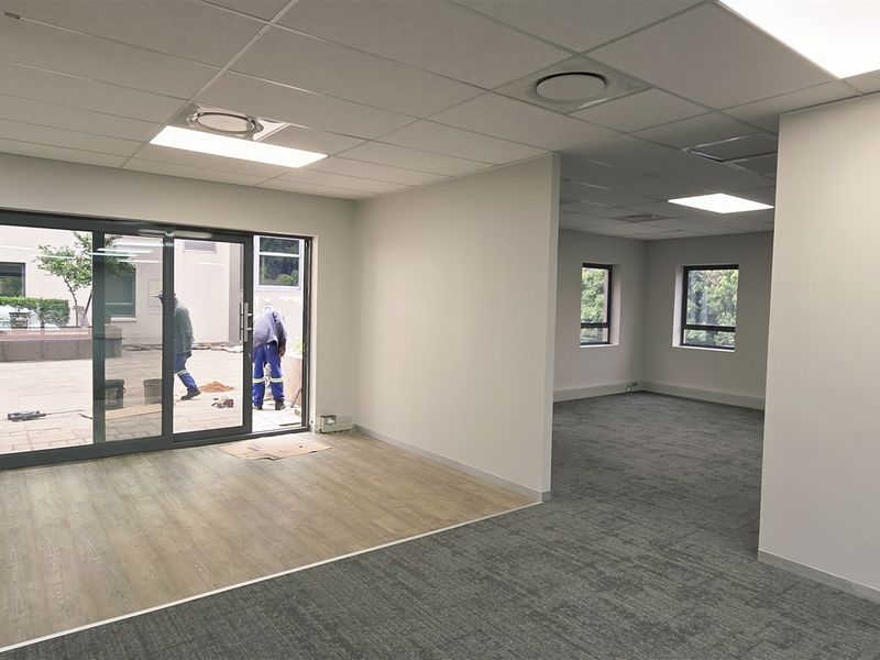 Spacious open-plan office area featuring a mix of carpet and wood-look vinyl flooring, recessed lighting, and direct access to an outdoor patio.