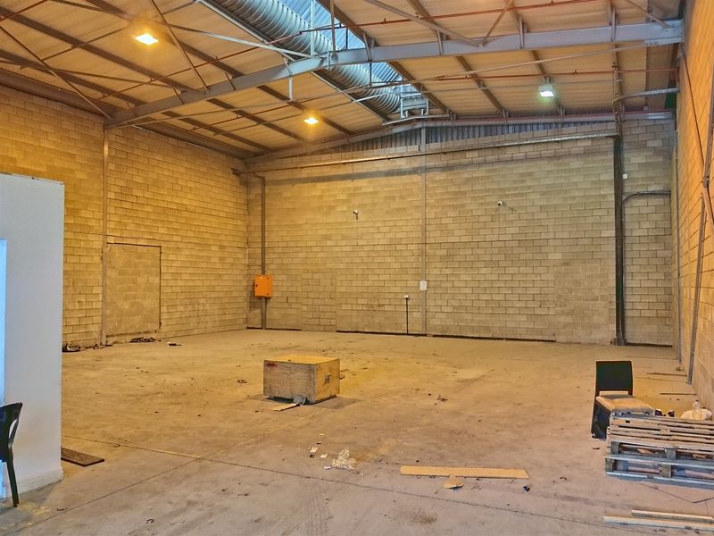 Spacious industrial warehouse unit featuring high ceilings with exposed steel trusses, concrete block walls, and durable concrete flooring, suitable for various commercial or storage uses.