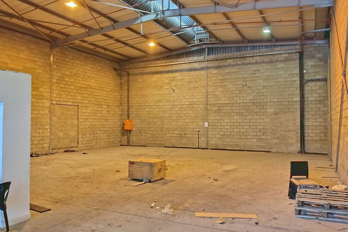 Spacious industrial warehouse unit featuring high ceilings with exposed steel trusses, concrete block walls, and durable concrete flooring, suitable for various commercial or storage uses.