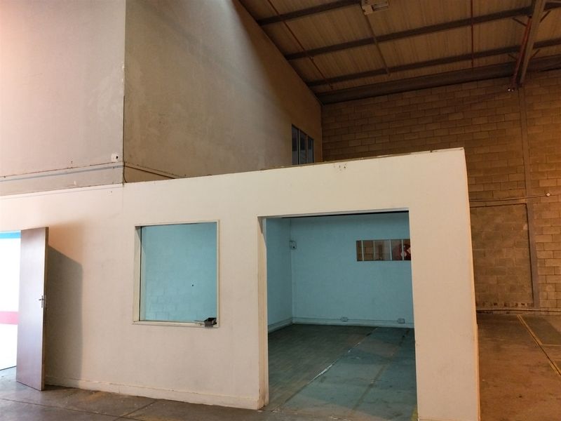 Industrial warehouse interior featuring a partitioned office enclosure, mezzanine level, and exposed brickwork, offering a versatile space for commercial or storage use.