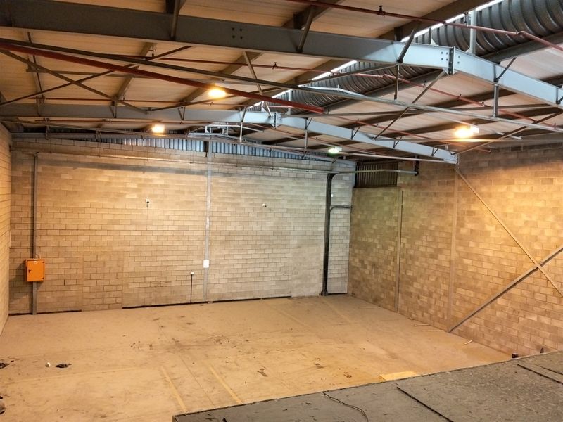 Spacious industrial warehouse unit featuring exposed steel roof trusses, concrete block walls, and functional sprinkler system, suitable for storage or light manufacturing.