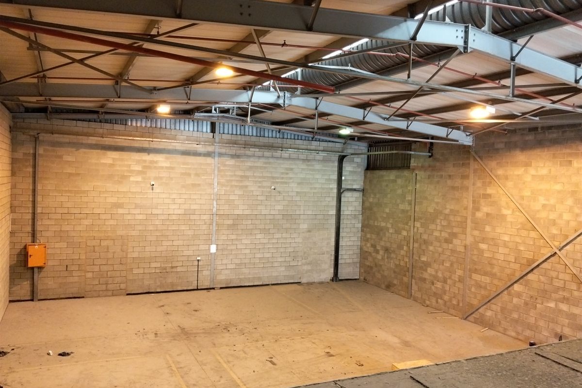 Spacious industrial warehouse unit featuring exposed steel roof trusses, concrete block walls, and functional sprinkler system, suitable for storage or light manufacturing.