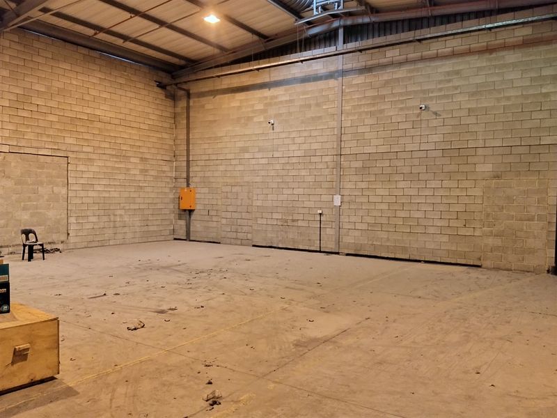 Spacious industrial utility area featuring exposed concrete block walls, high ceilings with steel trusses, and durable concrete flooring, suitable for storage or workshop use.