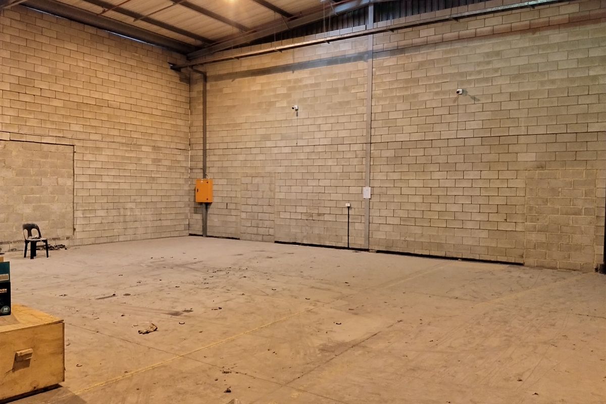 Spacious industrial utility area featuring exposed concrete block walls, high ceilings with steel trusses, and durable concrete flooring, suitable for storage or workshop use.