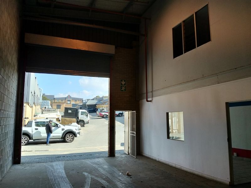 Industrial warehouse space featuring a large roller shutter door, high ceilings with fire safety infrastructure, and direct access to the exterior yard area.